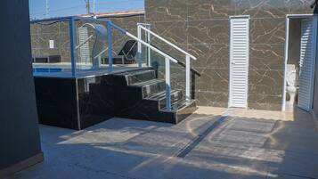 Uma área externa moderna com piscina envidraçada, escada de metal e porta que dá para um espaço coberto.