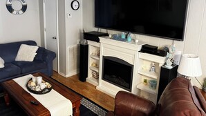 A living room with a fireplace, a large TV, a blue sofa, a brown leather chair, and a coffee table with a tray of snacks. - 2B/2B COZY BEACH GETAWAY IN OCEAN LAKES RESORT MYRTLE BEACH SC w/GOLF CART (Myrtle Beach)
