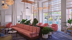 A spacious lobby with a large pink sofa, hanging wicker lamps, and potted plants.