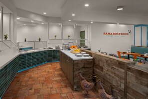 A restaurant interior with a counter, seating area, and a wall sign. - Luxe King Room w/ Balcony | Marina, Golf & Bar (Stuart)