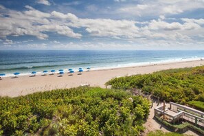 A beach with rows of blue umbrellas, a wooden deck, and a view of the ocean. - Direct Golf Course Access | Outdoor Pool & Gym (Stuart)
