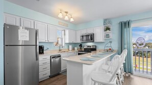 A modern kitchen with white cabinets, stainless steel appliances, and a bar area with white stools. - Gulf Shores West Beach Condo/3-Min Walk to Beach/Gulf Views/King Bed (Gulf Shores)