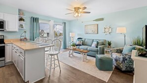 A modern kitchen with white cabinets, a central island, and a dining area with chairs. - Gulf Shores West Beach Condo/3-Min Walk to Beach/Gulf Views/King Bed (Gulf Shores)