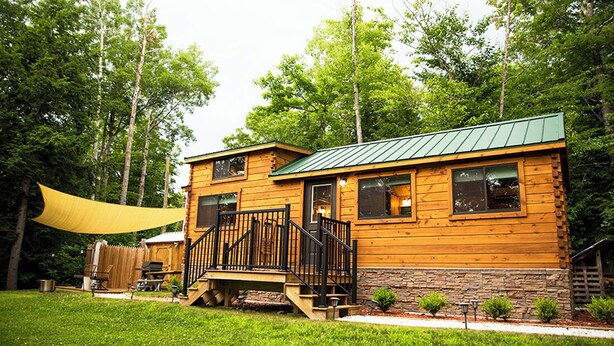A wooden cabin with a green roof, a deck, and a stone foundation. - Rivertop Retreat, with hot tub!- Luxurious tiny home in the White Mountains! (Bath)
