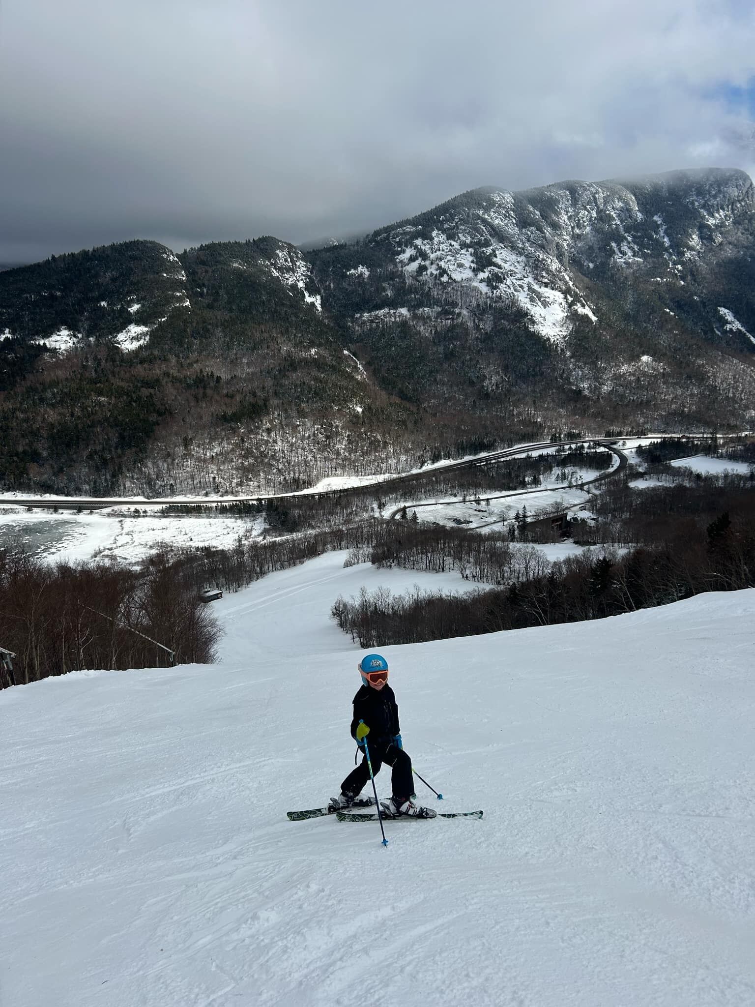 A person skiing down a snowy slope with a mountainous backdrop.