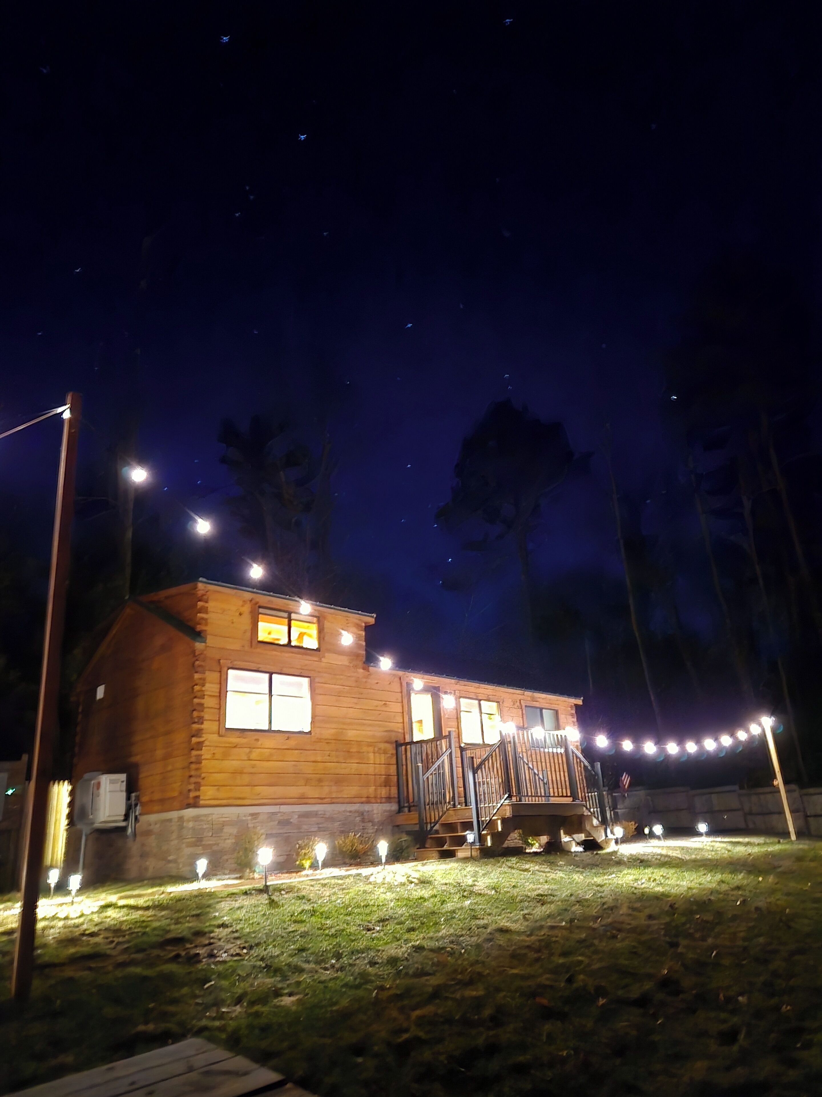 Eine Holzhütte mit Veranda, beleuchtet von Lichterketten und Straßenlaternen.