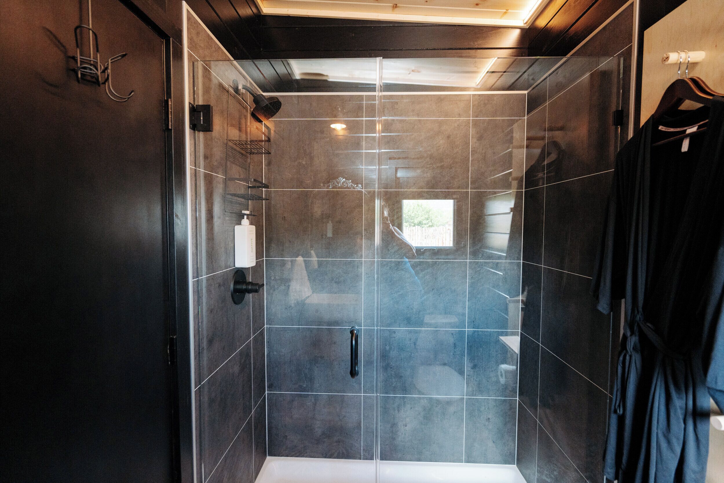A modern bathroom with a glass shower enclosure, a towel rack, and a robe hanging on the wall.