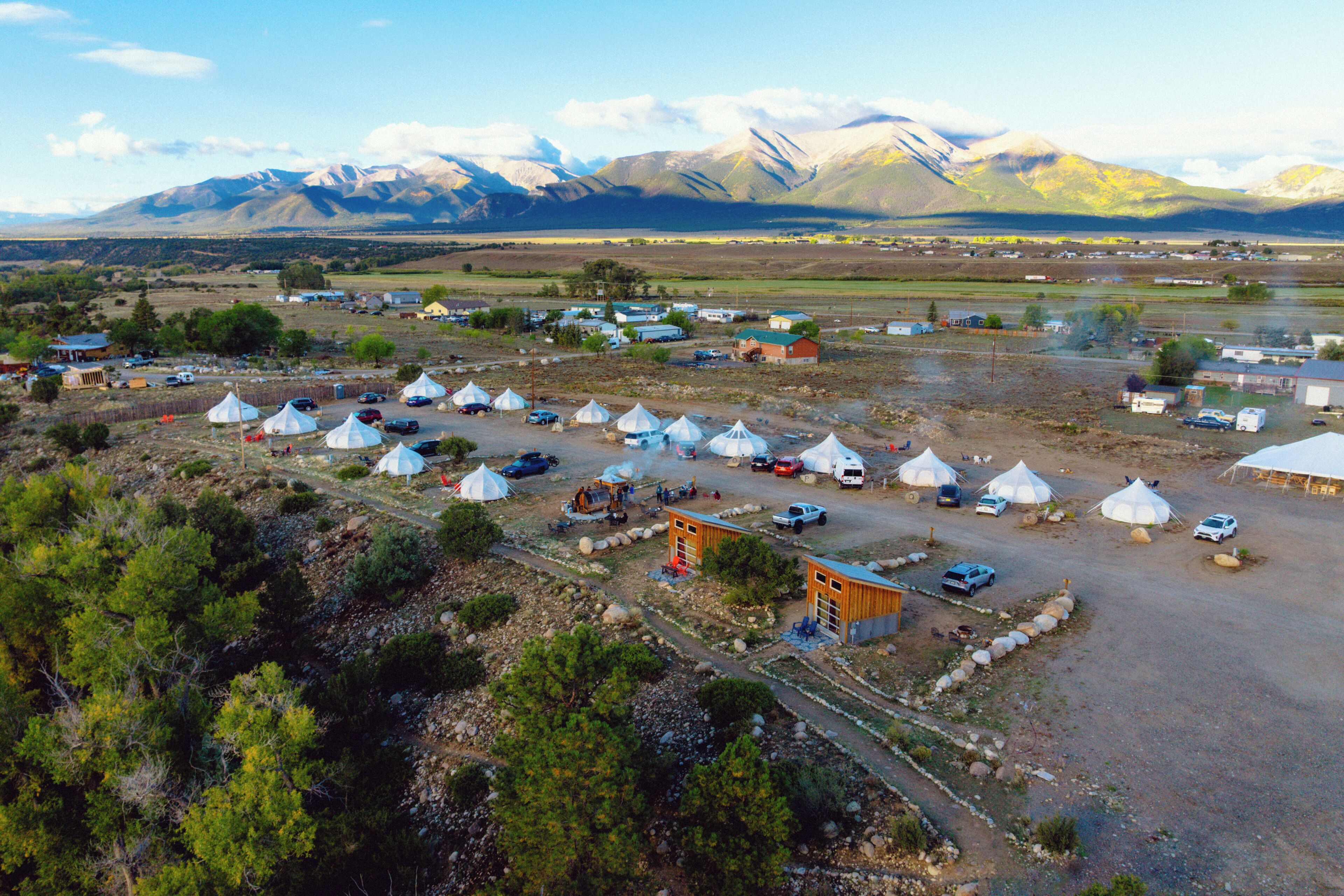 A campsite with yurts, vehicles, and a mountainous backdrop.