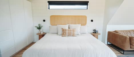A bedroom with a large bed, a headboard, bedside tables, a potted plant, and a brown sofa.