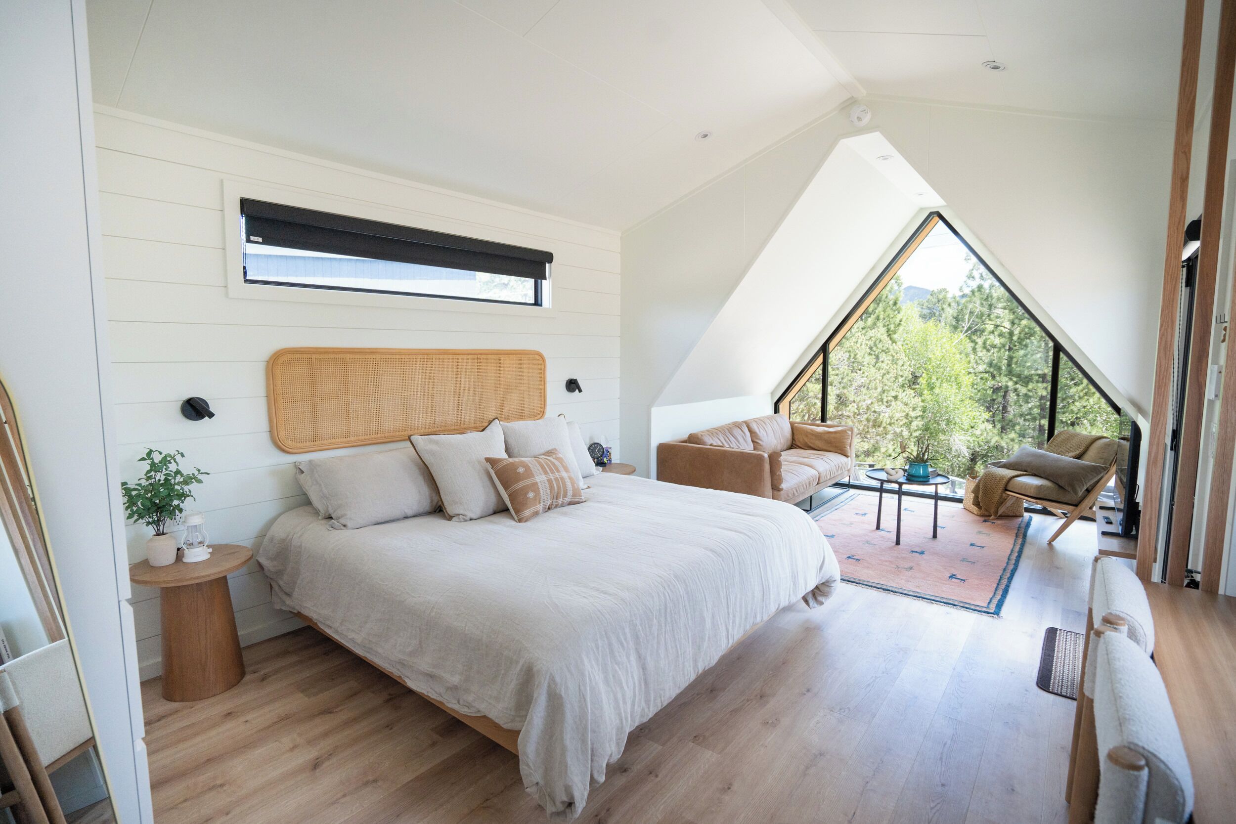 A bedroom with a large bed, a seating area with chairs, a small table, and a view through a large window.