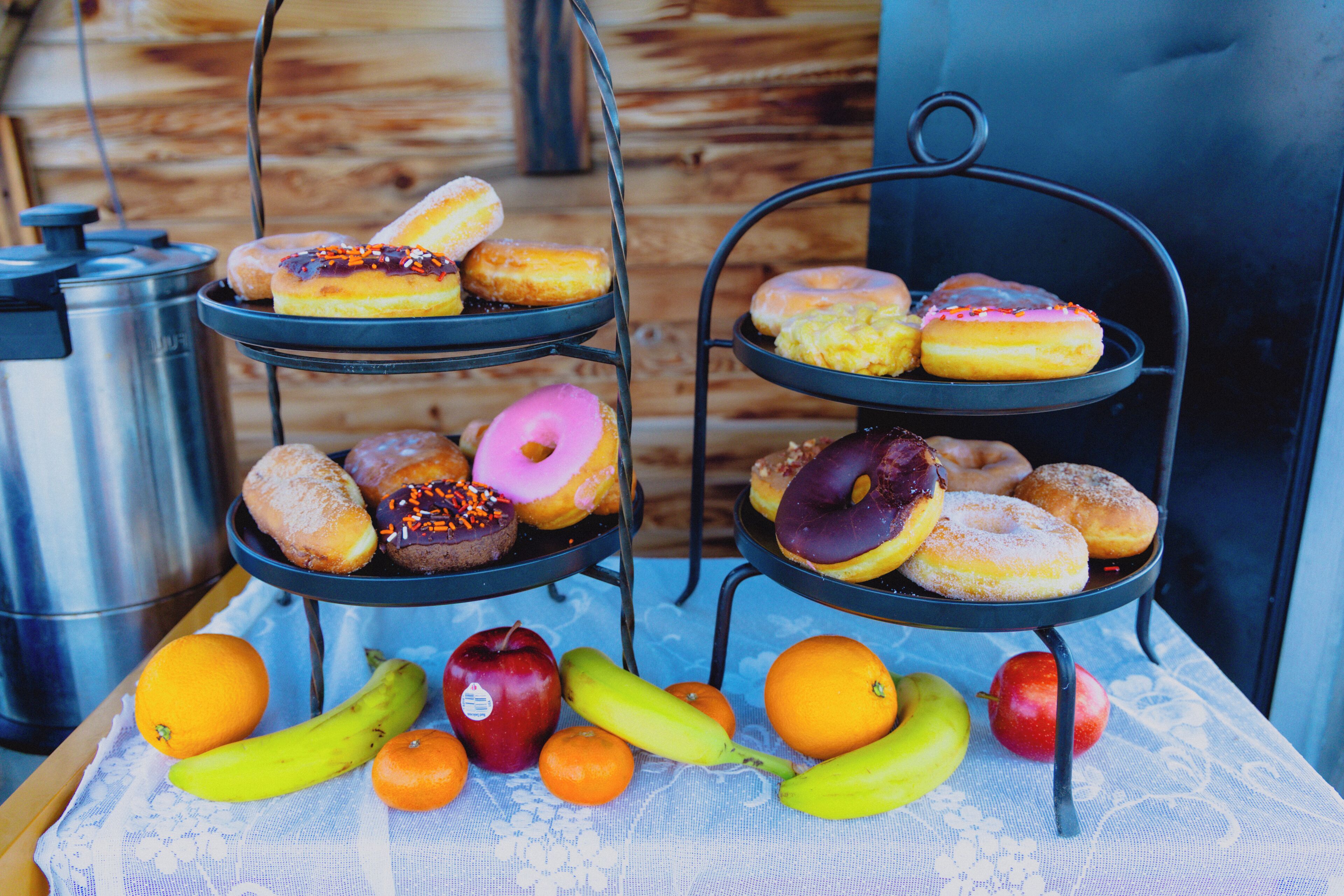 A table with a fruit arrangement and a three-tiered metal stand holding donuts.