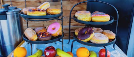Uma mesa com uma composição de frutas e um suporte de metal de três andares com donuts.