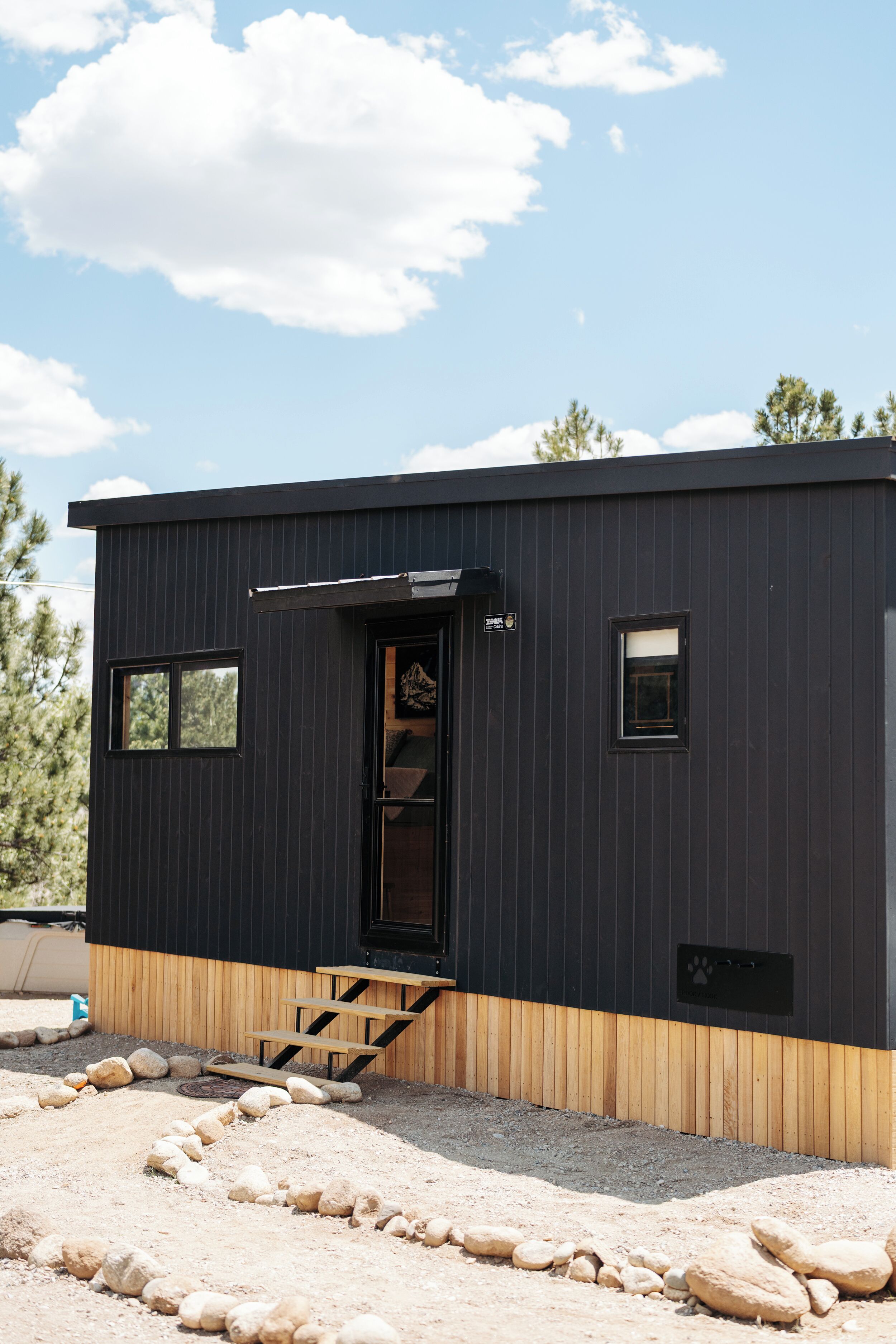 A modern building with a dark exterior, a wooden lower section, a small porch, and a clear sky.