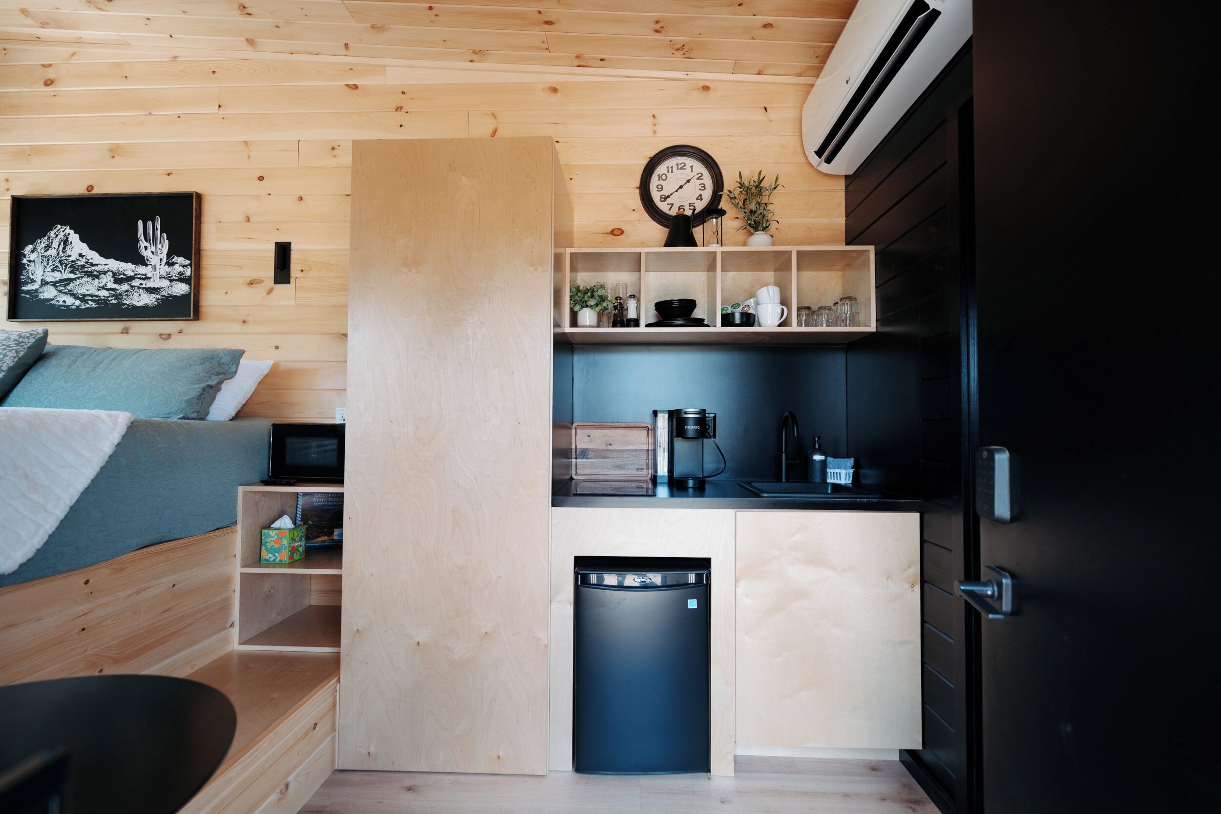 A compact kitchen with a dishwasher, a clock, and a small shelf with various items.