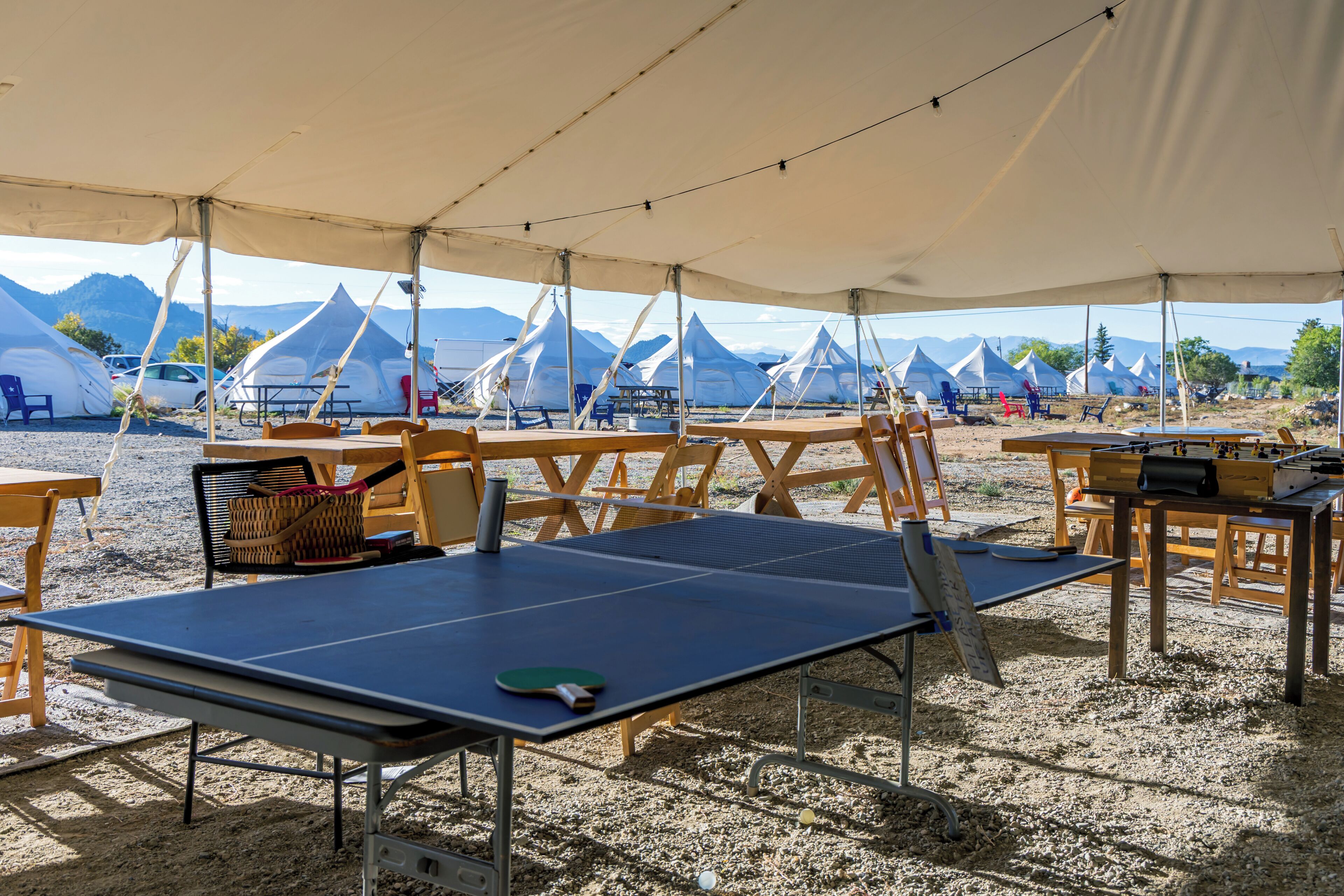 A tented area with ping pong tables, chairs, and tables.