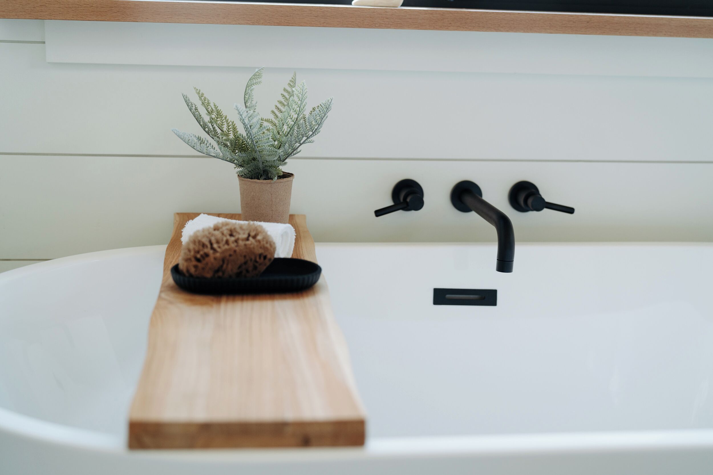 Une baignoire avec un plateau en bois, une éponge et une plante en pot.