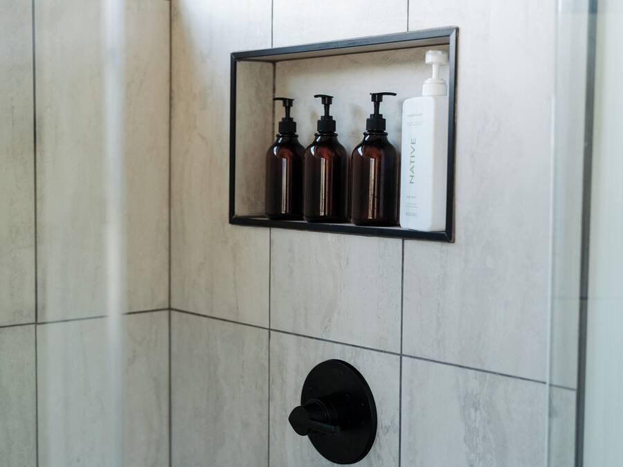 A bathroom with a tiled wall, a black sink, and a shelf with three bottles.
