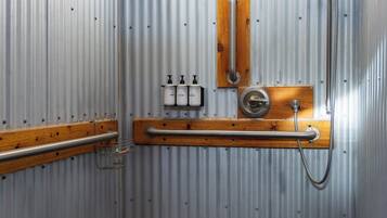 Un baño pequeño con paredes de metal, techo de madera, ducha, inodoro y un estante con artículos de aseo.