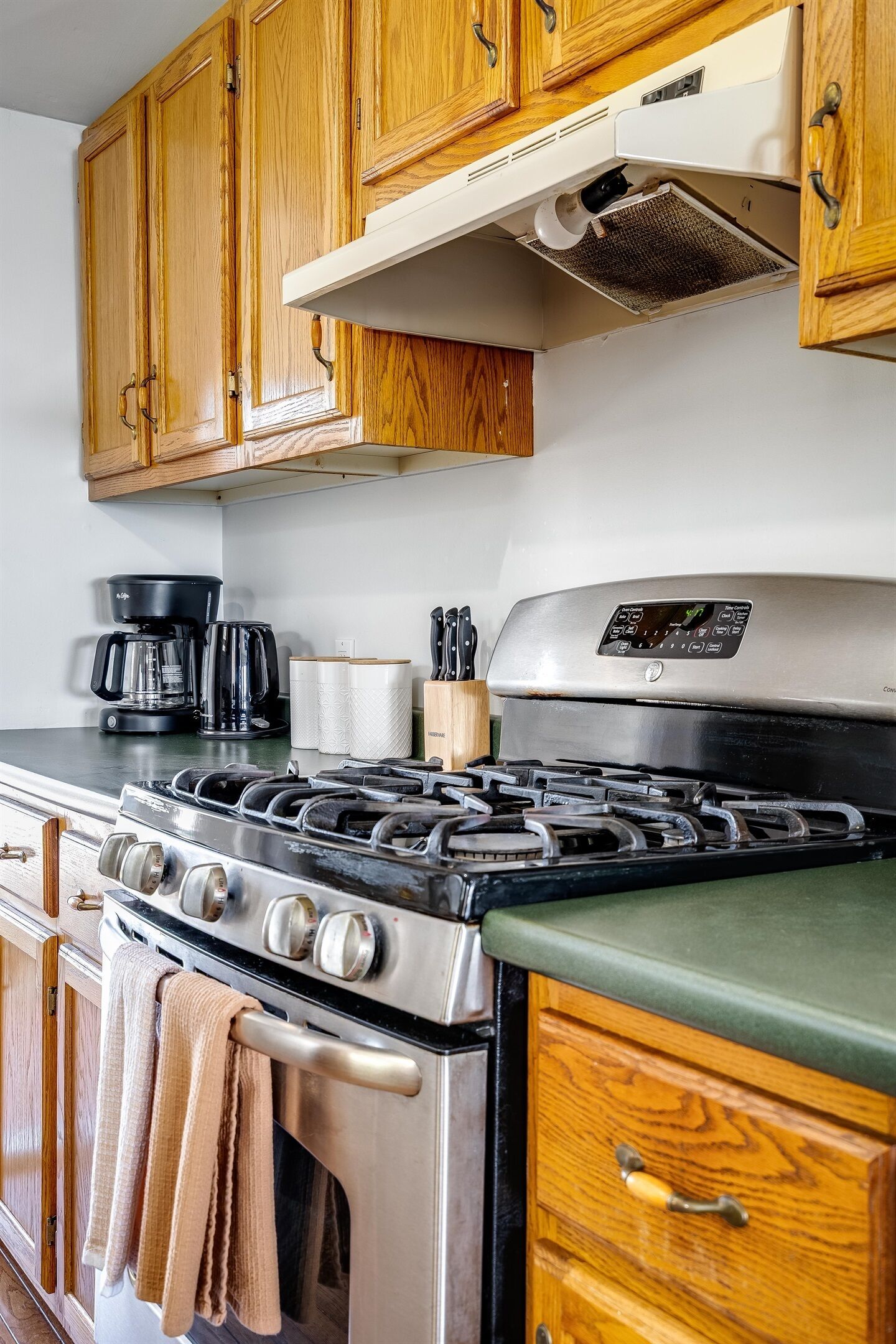 A kitchen with wooden cabinets, a stainless steel stove, a coffee maker, and a range hood.