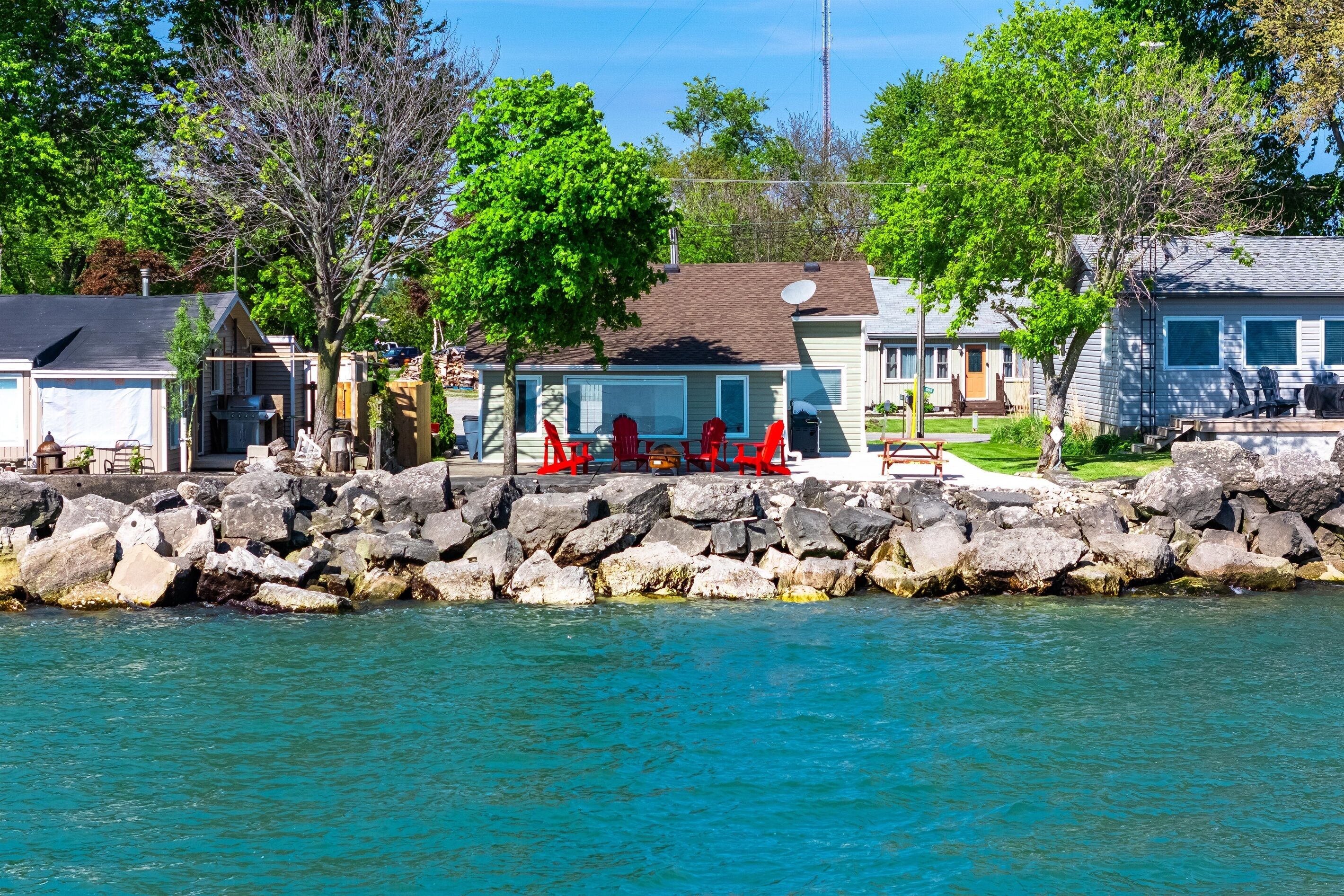 A waterfront property with a dock, a covered outdoor seating area with red chairs, and a house with a satellite dish.