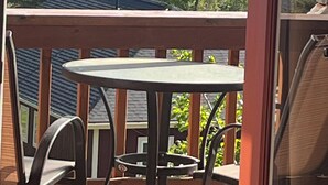 A balcony with a table and chairs, overlooking a forested area and distant mountains.