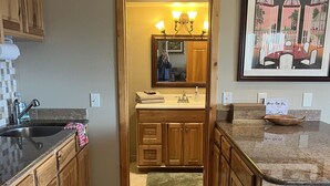 A kitchen with wooden cabinets, a sink, and a countertop. There is a framed picture on the wall and a sign on the countertop.