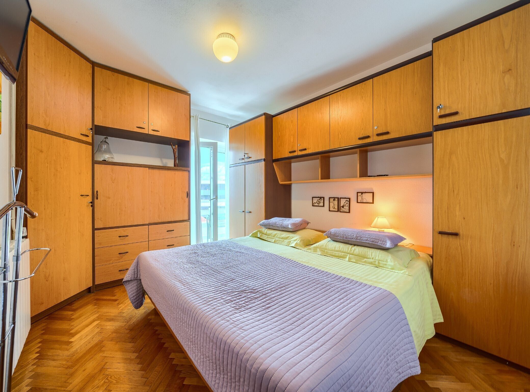 Une chambre avec des armoires en bois, un lit recouvert d’une courtepointe matelassée et une lampe fixée au mur.