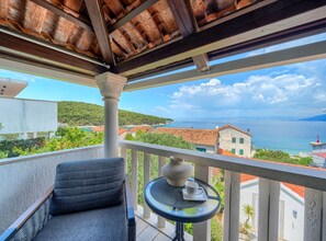 A balcony with a chair, a small table with a cup, and a view of the sea and buildings. - Three bedroom Apartment with terrace and sea view (Postira)