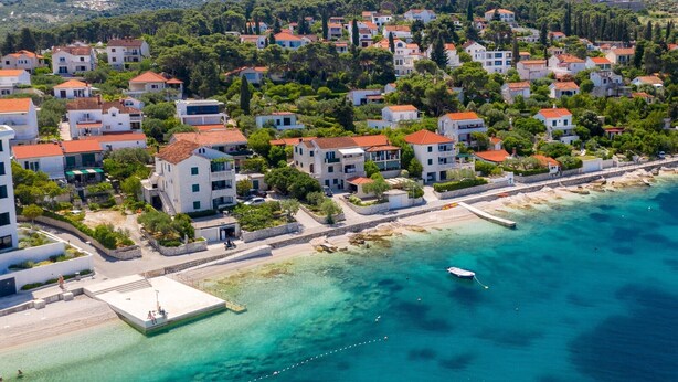Vista aérea de una zona residencial costera con casas, una playa y aguas azules cristalinas.
