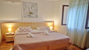 A hotel room with a large bed, two bedside tables with lamps, a floral wall decoration, and a window with curtains.