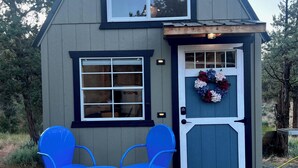 Een klein huis met een veranda, twee blauwe stoelen en een krans op de deur.