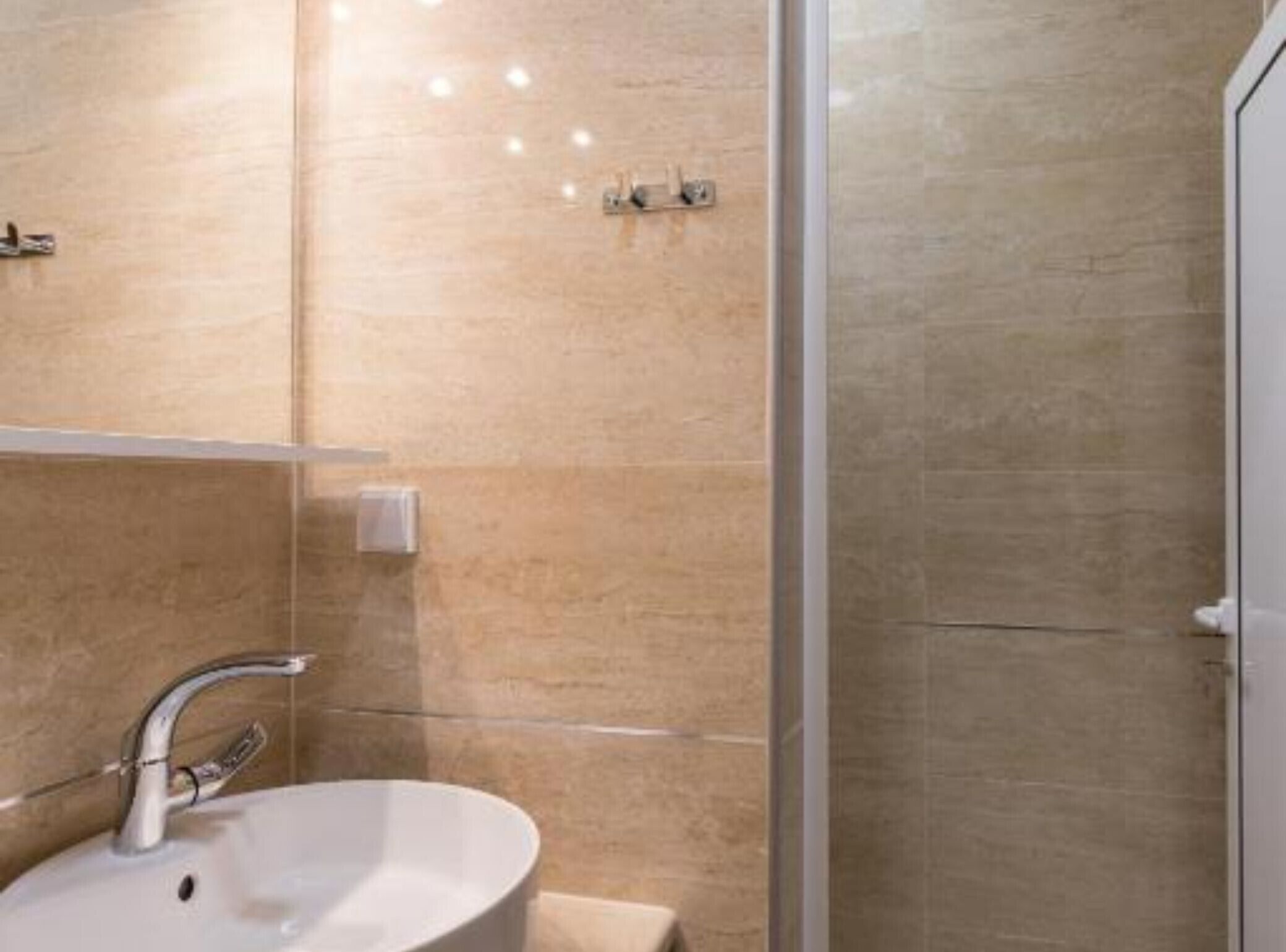 Un baño con lavamanos blanco, un espejo y zona de ducha.