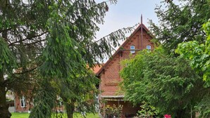 Ein Ziegelgebäude mit geneigtem Dach, umgeben von einem gepflegten Garten mit verschiedenen blühenden Pflanzen und Bäumen.