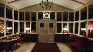 Ein gemütliches Zimmer mit großem Fenster, einer Chandelüster und einem Weihnachtsgesteck.