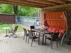 En udendørs terrasse med en murstensvæg, et bord, stole og en gyngestol.