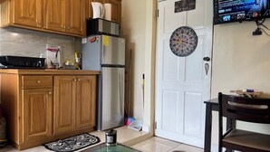 A kitchen with wooden cabinets, a microwave, a refrigerator, a dartboard, a television, and a remote control on a glass table. - Cozy 1-bedroom apartment with WiFi, Pool near the Airport & Store Bay Beach (Crown Point)