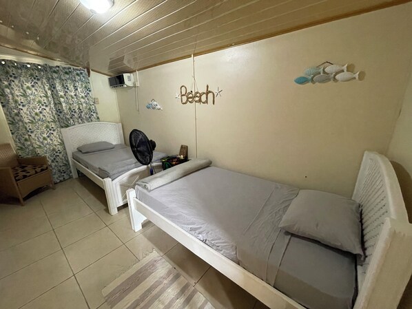 Een slaapkamer met twee eenpersoonsbedden, een plafondventilator, een luchtverkoeler aan de muur en decoratieve muurkunst van vissen.