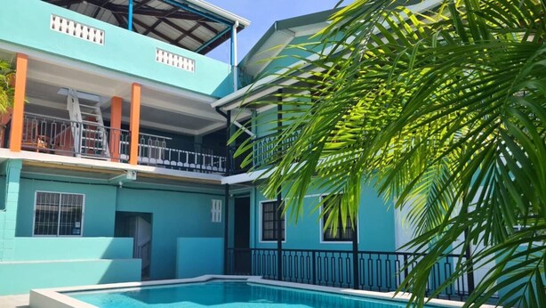 A two-story building with a swimming pool in front. - Cozy 1-bedroom apartment with WiFi, Pool near the Airport & Store Bay Beach (Crown Point)
