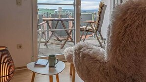 A cozy room with a large window, a fluffy chair, a small table with a book and a mug, and a lamp. - Refugium Möhneseeblick. our cozy vacation apartment.central and yet quiet. (Möhnesee)