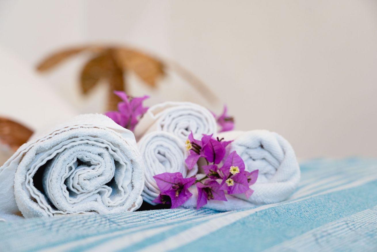 Rolled white towels and purple flowers on a striped fabric.