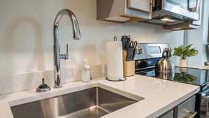 Una cocina moderna con un lavamanos de acero inoxidable, un microondas integrado y un hervidor en la encimera.
