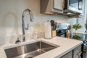 A modern kitchen with a stainless steel sink, a built-in microwave, and a kettle on the countertop.