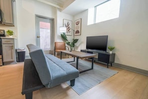 Un salon avec un canapé, une table basse, un téléviseur et une plante.