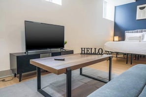 Une chambre dâhĂŽtel moderne Ă©quipĂ©e dâun tĂ©lĂ©viseur Ă Ă©cran plat, dâune table basse en bois, dâun lit et dâune enseigne lumineuse avec le mot « HELLO ».