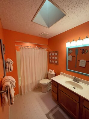 Un baño con una pared naranja, un inodoro blanco, un lavabo blanco con espejo y una cortina de ducha.