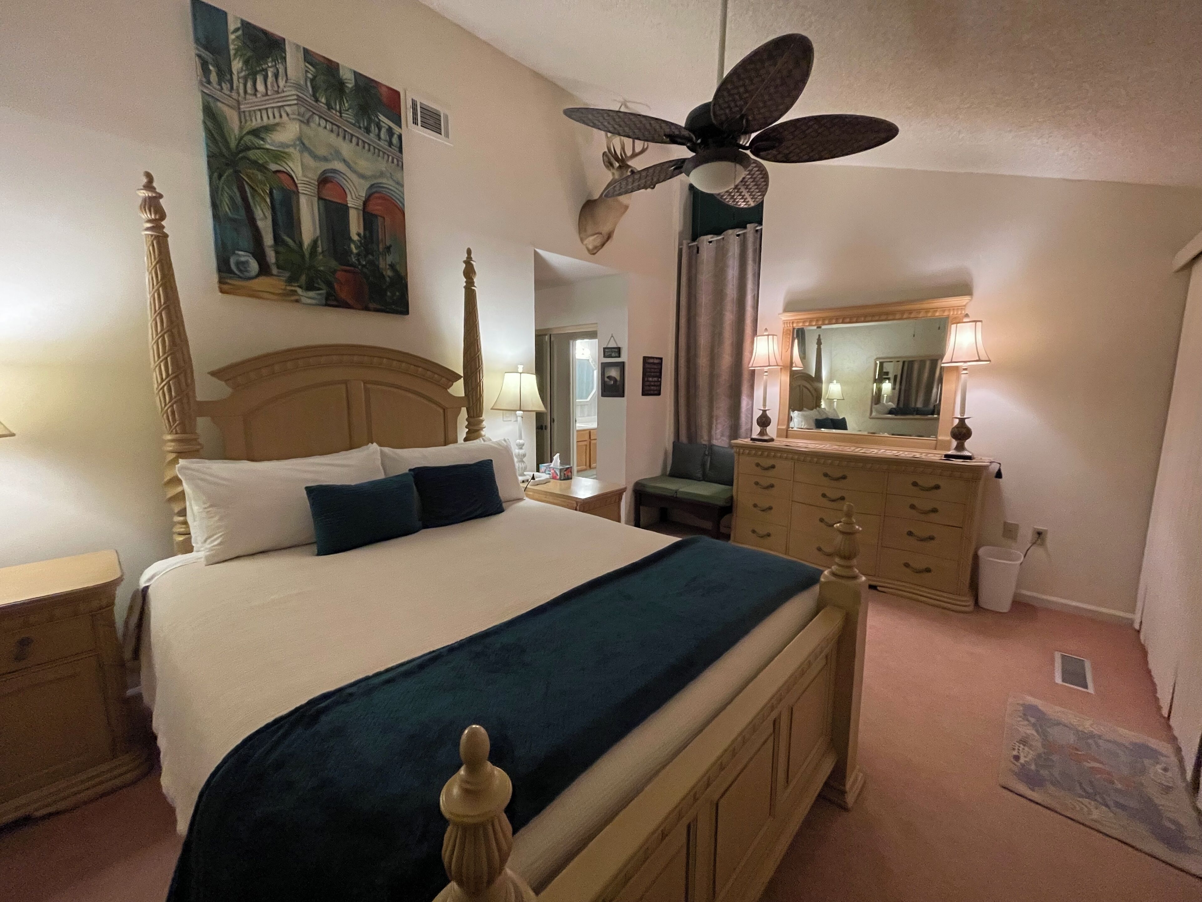 Ein Schlafzimmer mit einem Himmelbett, einem Deckenventilator, einer Kommode und einem Bild an der Wand.