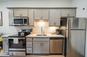 A modern kitchen with grey cabinets, a stainless steel refrigerator, a microwave, an oven, and a dishwasher.