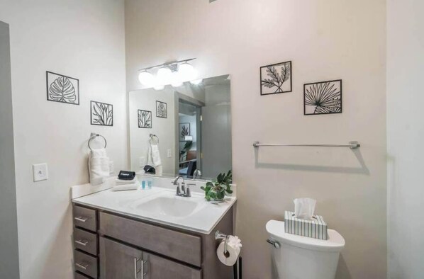Une salle de bain Ă©quipĂ©e dâun lavabo, dâun miroir, dâun porte-serviettes, de toilettes et dâĆuvres dâart dĂ©coratives sur les murs.
