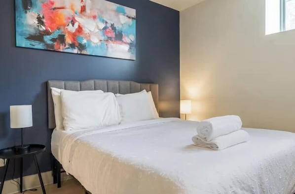 A hotel room with a bed, a nightstand, a lamp, and a painting on the wall.