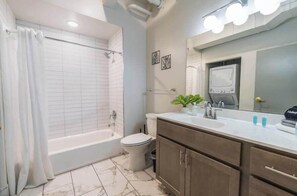 Ein Badezimmer mit einer Badewanne, Toilette, Waschtisch mit Spiegel und Duschvorhang.
